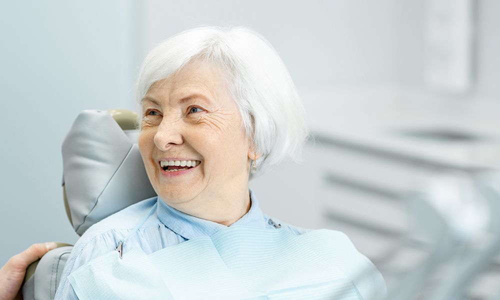 Hermosa anciana con una sonrisa saludable sentada durante la consulta con el dentista en el consultorio dental