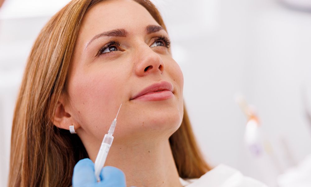 Mujer con tratamiento de belleza en el consultorio médico, médico aplicando rellenos faciales.